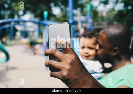 Vater nimmt Selfie durch Smartphone, während küssen Sohn an parken Stockfoto