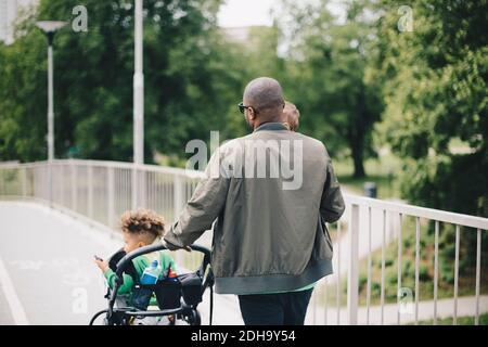 Rückansicht des Vaters, der den Kinderwagen beim Gehen mit schiebt Söhne auf der Brücke Stockfoto