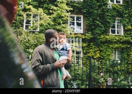 Liebevoller Vater küsst Sohn, während er gegen Zaun in der Stadt steht Stockfoto