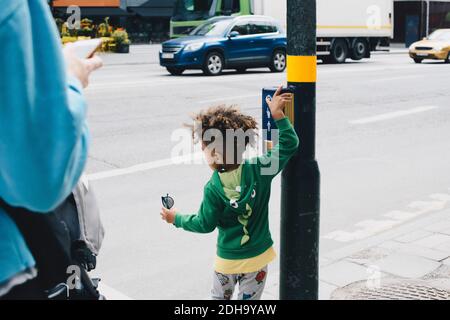 Rückansicht des Jungen mit Mutter Druckknopf auf Fußgänger Überquerung Schild in der Stadt Stockfoto