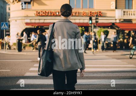 Rückansicht einer Frau, die die Straße in der Stadt überquert Stockfoto