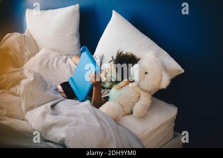 High-Winkel-Ansicht des Jungen mit Stofftier liegen, während Mit einem digitalen Tablet auf dem Bett zu Hause Stockfoto