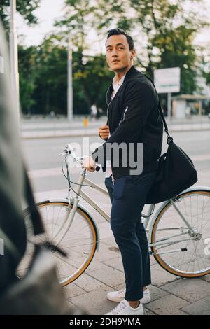 Junger Mann schaut weg, während er Fahrrad in der Stadt hält Stockfoto
