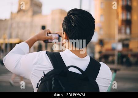 Rückansicht eines jungen Mannes, der durch das Mobiltelefon fotografiert Stadt Stockfoto