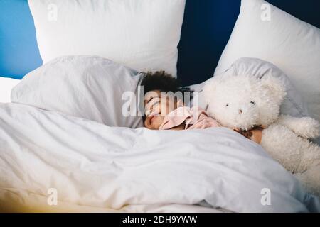 Lächelnder Junge schläft mit Teddybär auf dem Bett zu Hause Stockfoto