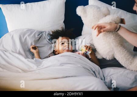 Lächelnder Junge, der Mutter ansieht, während er auf dem Bett liegt Zu Hause Stockfoto