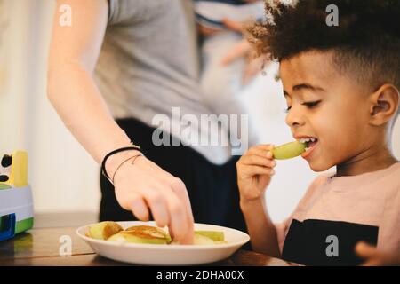 Junge mit Essen, während sie von der Mutter zu Hause sitzen Stockfoto