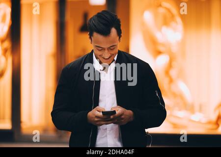 Lächelnder junger Mann mit Handy, während er im Licht stand Stadt Stockfoto