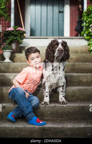 Porträt eines lächelnden Jungen, der mit englischem Springer Spaniel sitzt Treppen im Hinterhof Stockfoto