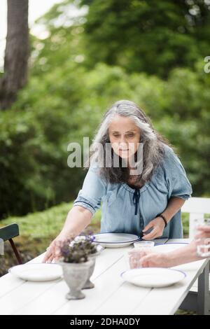 Ältere Paare, die Teller auf dem Tisch im Hinterhof anordnen Stockfoto