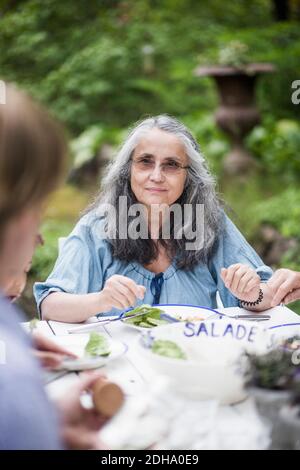 Ältere Mutter schaut auf reifen Sohn sitzen im Hinterhof Stockfoto