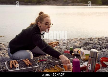 Junge Frau, die während des Sonnenuntergangs am Strand Essen zubereitete Stockfoto