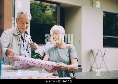 Lächelnde ältere Frau zeigt dem Mann beim Einkaufen Textilien Markt in der Stadt Stockfoto
