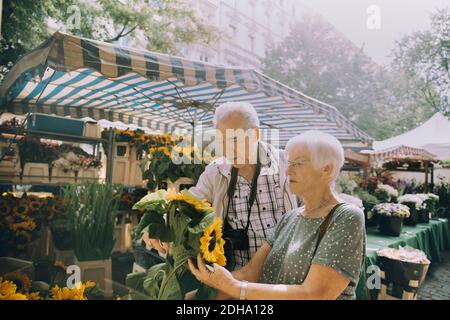 Ältere Frau hält Sonnenblumen beim Einkaufen mit Mann bei Blume Markt in der Stadt Stockfoto