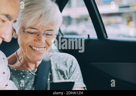 Lächelnde ältere Frau, die dem Mann während des Sitzens das Handy zeigt Im Auto Stockfoto