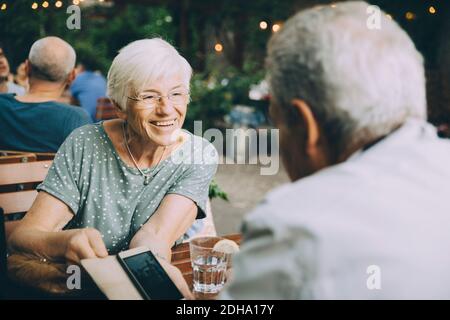Lächelnde Frau, die dem älteren Mann während des Sitzens das Handy zeigt Im Restaurant in der Stadt Stockfoto