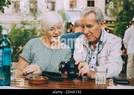 Älterer Mann, der der Frau die Kamera zeigt, während er im Restaurant sitzt In der Stadt Stockfoto