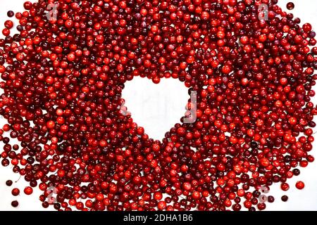 Ein herzförmiger Rahmen aus Preiselbeeren. Ein weißes Fenster, umgeben von vielen roten Perlen. Stockfoto