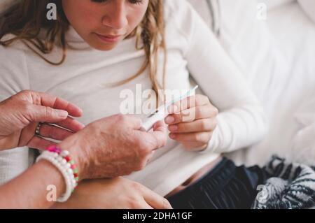 Zugeschnittenes Bild der Großmutter, die der Enkelin im Schlafzimmer ein Thermometer zeigt Stockfoto