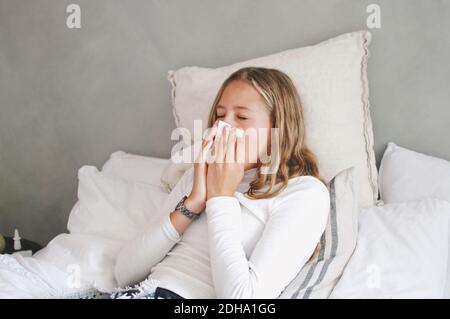 Mädchen bläst Nase, während auf dem Bett zu Hause liegen Stockfoto