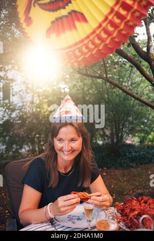 Glückliche reife Frau, die Krebse isst, während sie am Esstisch sitzt Während Gartenparty Stockfoto