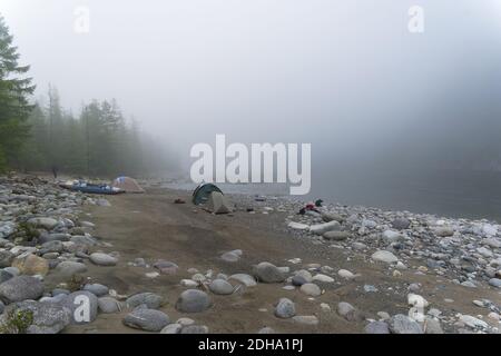 Ferienlager am Ufer eines Bergflusses an einem nebligen Morgen. Stockfoto