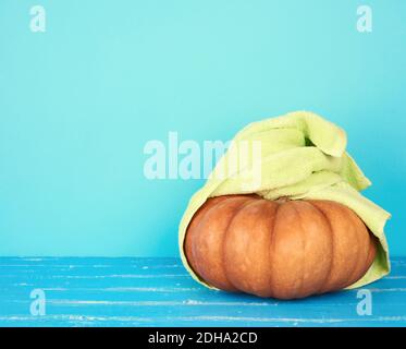 Runder orangefarbener Kürbis in ein grünes Frottee-Handtuch gewickelt Stockfoto