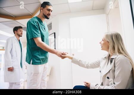 Seitenansicht der Patientin, die sich mit dem jungen Mann die Hände schüttelt Krankenschwester im Krankenhaus Stockfoto