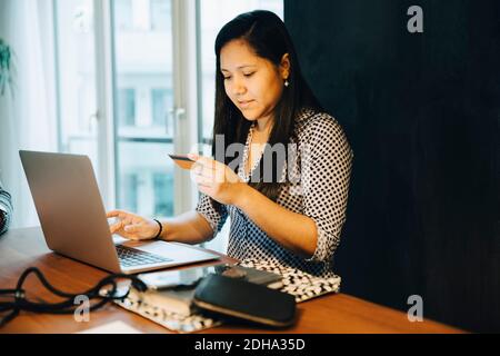 Frau mit Kreditkarte beim Online-Shopping auf Laptop, während Zu Hause sitzen Stockfoto