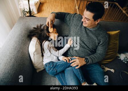 Hohe Winkelansicht des Vaters, der die Haare seiner Tochter während des Sitzens kämmt Auf dem Sofa zu Hause Stockfoto