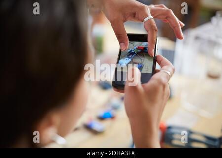 Zugeschnittenes Bild von jungen weiblichen Ingenieur berühren mobilen Bildschirm während Fotografieren Modell in der Werkstatt Stockfoto