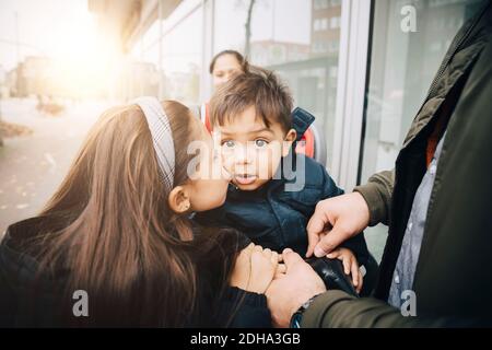 Schwester küsst sich auf die Wange des Bruders, während sie auf dem Fahrradsitz sitzt Mit Vater in der Stadt Stockfoto