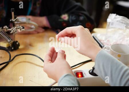 Kurzgeschnittene Hände junger Technikerin, die elektrische Bauteile hält Werkstatt Stockfoto