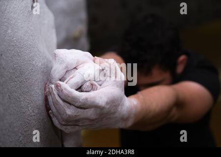 Männliche Hände mit Magnesiumpulver verschmiert und greifen einen Griff einer Kletterwand. Nahaufnahme. Stockfoto