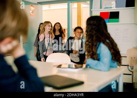 Lächelnde männliche und weibliche Schüler, die in den Klassenzimmer eintreten Stockfoto