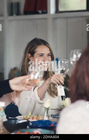 Lächelnde junge Frau, die während der Mittagsparty mit Freunden anstößt Stockfoto