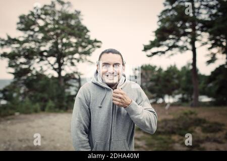 Portrait von lächelnden jungen Mann Zipping Kapuzen Sweatshirt im Rücken Hof Stockfoto