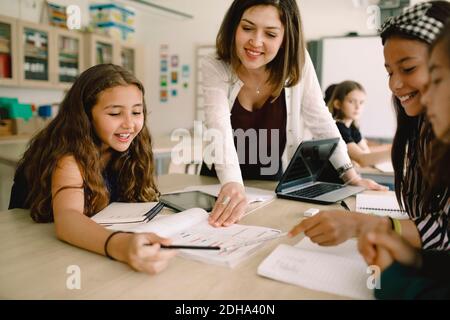 Studenten mit lächelnder Tutorin, die am Tisch aus dem Buch lernt Im Klassenzimmer Stockfoto
