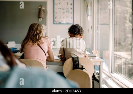 Rückansicht der männlichen und weiblichen Studenten, die am Tisch sitzen Im Klassenzimmer Stockfoto