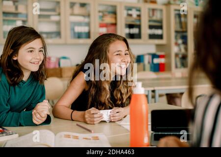 Lächelnde Schülerin mit Papier sitzt von einem Freund im Klassenzimmer Stockfoto