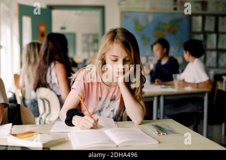 Studentin mit der Hand auf dem Kinn studieren aus Buch, während Sitzen im Klassenzimmer Stockfoto