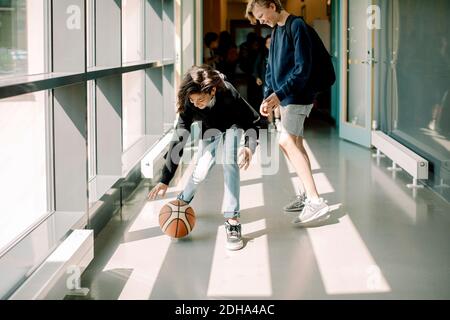 Lächelnde männliche Schüler spielen mit Basketball im Schulkorridor Stockfoto