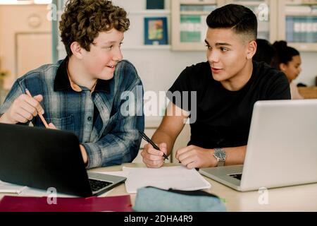 Männliche Schüler sprechen, während sie am Tisch im Klassenzimmer sitzen Stockfoto