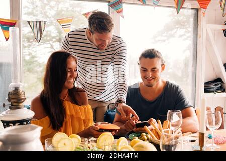 Junge Männer und Frauen mit Handy am Esstisch Stockfoto