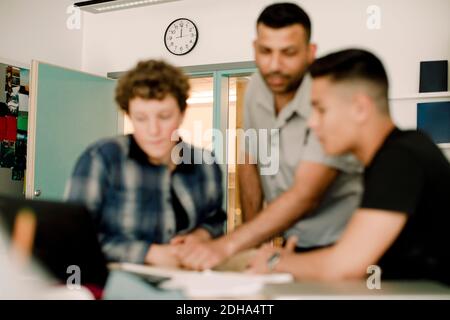 Männlicher Lehrer, der mit männlichen Schülern diskutiert, während er im Klassenzimmer steht Stockfoto