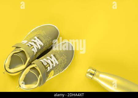 Graue Sneakers und Flasche mit Wasser auf gelbem Hintergrund. Konzept für gesundes Leben, Sport und Training, Draufsicht, Kopierraum. In trendigen Farben getönt Stockfoto