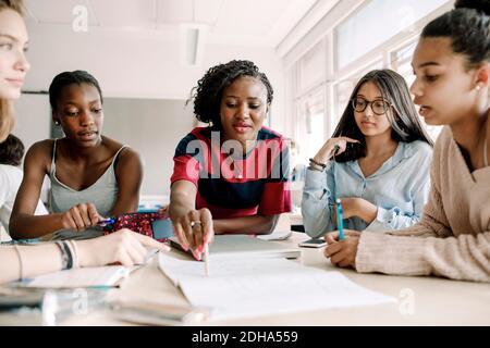 Lehrerin erklärt, während Schülerinnen am Tisch im Klassenzimmer studieren Stockfoto