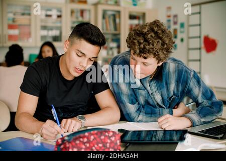 Männliche Schüler, die am Tisch studieren, während sie im Klassenzimmer sitzen Stockfoto