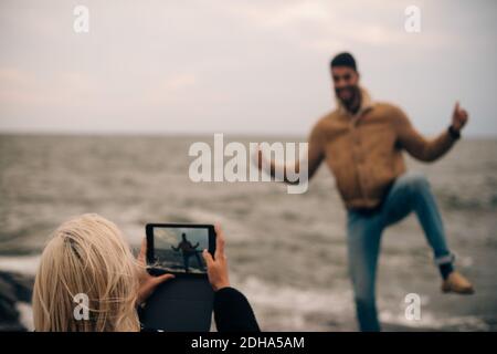 Junge Frau fotografiert Mann auf digitalen Tablet am Strand Stockfoto