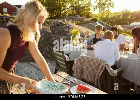 Frau pflücken Wassermelone Scheibe, während Freunde essen auf genießen Picknicktisch am Hafen Stockfoto